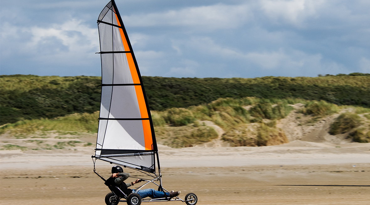 Person sitting in a wheeled three-wheeled buggy with a sail, racing on flat sand